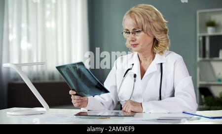 Donna bionda che esamina l'immagine dei raggi X, la professione medica, la diagnosi Foto Stock