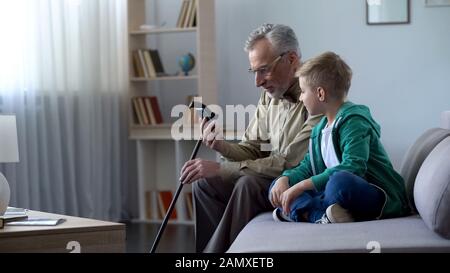 Nonno che tiene il telefono, ragazzo che lo aiuta a conoscere le nuove tecnologie Foto Stock