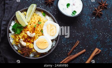 Uovo indiano Biryani o eun riso vista dall'alto su sfondo scuro. Uovo - Biryani riso Basmati cotto con masala uova arrosto e spezie, servito con yogurt. Copia spazio per il testo Foto Stock