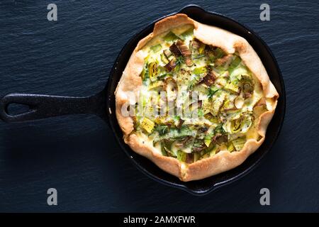 Sano concetto di cibo fatto in casa biologica Leek quiche in padella ghisa su lavagna in pietra di ardesia nera Foto Stock