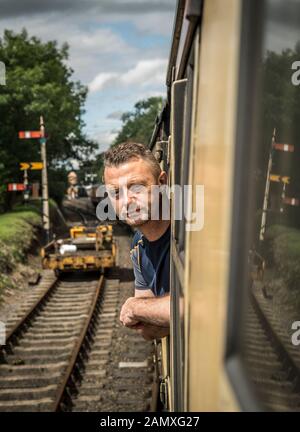 Uomo che guarda fuori dalla carrozza ferroviaria d'epoca a bordo del treno a vapore britannico, Severn Valley Heritage Steam Railway. Foto Stock