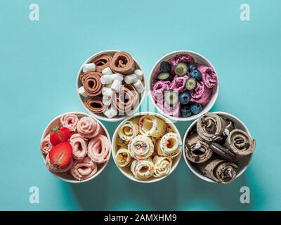 Gelati arrotolati in tazze coniche su sfondo blu. Diversi rotoli ghiacciati, vista dall'alto o piatto. Gelato laminato in stile thailandese Foto Stock