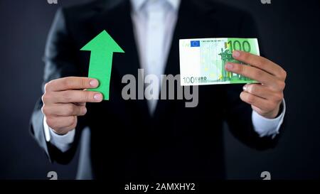 Uomo d'affari che mostra banconote in euro e il segno della freccia verde, la crescita della valuta, il reddito Foto Stock