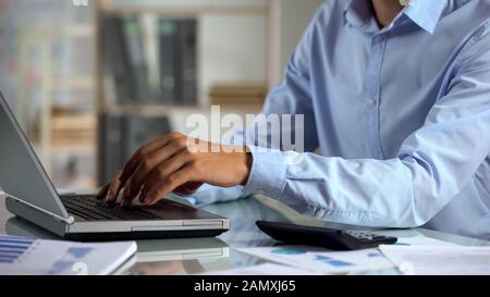 Uomo d'affari che fa rapporto di vendite dell'azienda, digitando i dati sul laptop, progetto dell'ufficio Foto Stock