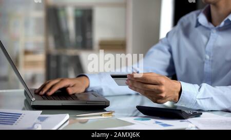 Amministratore che immette il numero della carta sul laptop dell'ufficio, lo shopping online, il banking Foto Stock