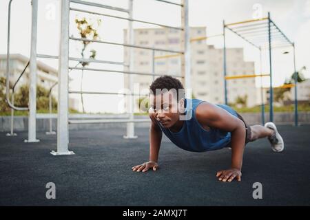 Montare il giovane americano africano uomo al lavoro su crossfit training di forza facendo spingere ups al parco calisthenics Foto Stock