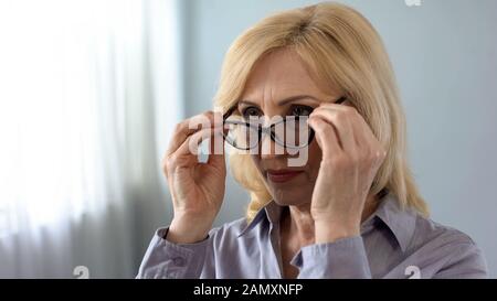 Senior serio businesswoman mettere su occhiali di fronte allo specchio, salute Foto Stock