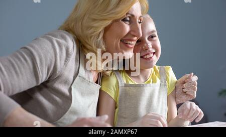 Simpatica nipote e sua nonna ridendo e abbracciando mentre cuocendo, la famiglia Foto Stock