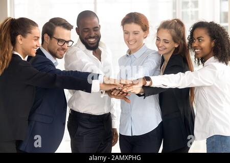 I dipendenti multietnici eccitati si accatastano le mani mostrando supporto e unità Foto Stock