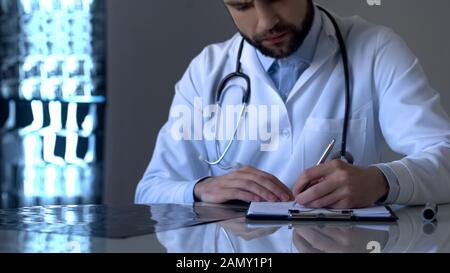 Medico esperto che esamina i raggi X e scrive la diagnosi in forma medica, salute Foto Stock