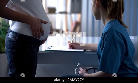 Giovane medico che scrive giù le note dopo l'esame della donna incinta, madre futura Foto Stock