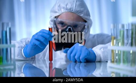 Scienziato in maschera di gas che tiene la provetta con sostanza pericolosa, rischio biologico Foto Stock