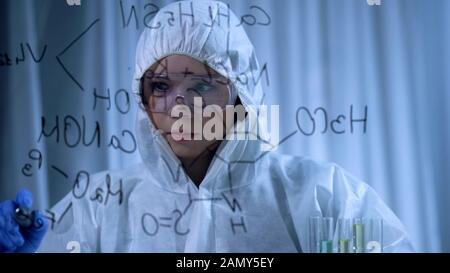 Farmacia femminile in tuta protettiva scrivere formula chimica strutturale a bordo Foto Stock