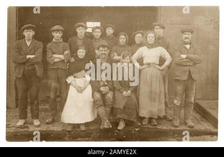 Edwardian fotografia di gruppo di giovani ragazze e ragazzi con gli uomini più anziani, eventualmente sorveglianti,vestito in abiti da lavoro - zoccoli, scialli. Questi sono probabilmente i lavoratori del mulino come una ragazza ha una cinghia con forbici in loro visto nel mulino altro lavoratore foto possibilmente Lancashire, Inghilterra, Regno Unito, circa 1910 Foto Stock