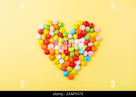 Misto di caramelle colorate su sfondo giallo. Forma del cuore Foto Stock