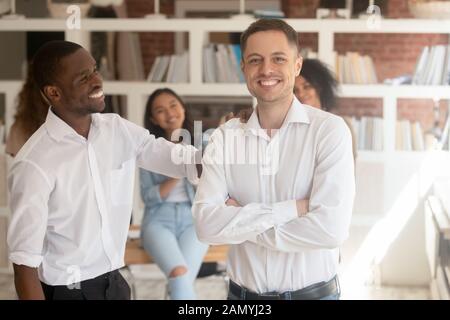 Uomini d'affari multirazziali eccitati che si pongono insieme in ufficio Foto Stock