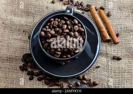 Nero caffè tazza piena di caffè organico fagioli e bastoncini di cannella sul panno di lino - immagine Foto Stock