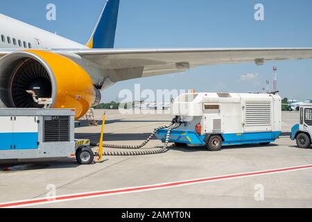 Grande e moderno piano commerciale parcheggiata su una pista di aeroporto e collegato a massa alimentazione unità di alimentazione. La manutenzione degli aeromobili e servizio check-up prima Foto Stock