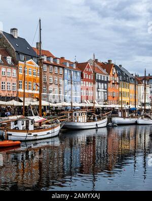 Danimarca, Copehagen, Nyhavn, ormeggiate barche & Porto nuovo waterfront rivestiti di colorate case a schiera, bar, caffetterie e ristoranti. Foto Stock
