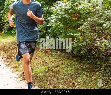 Un high school boy è in esecuzione su un percorso sterrato in un parco locale durante il cross country practice. Foto Stock