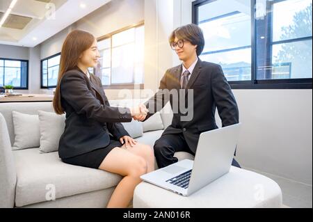 La gente di affari si stringono la mano su una scrivania con un computer nella parte posteriore Foto Stock