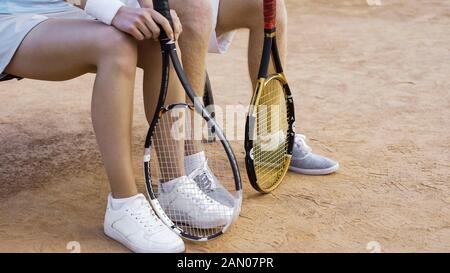 Giovani giocatori di tennis maschi e femmine in attesa di partita su panchina, gambe da vicino Foto Stock