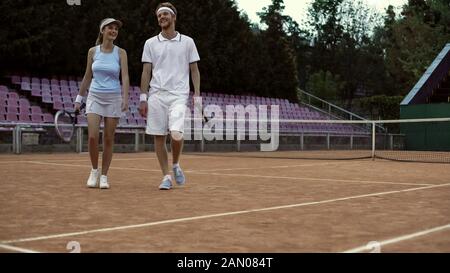 Coppia sorridente positiva che cammina sul campo da tennis dopo l'allenamento, stile di vita attivo Foto Stock