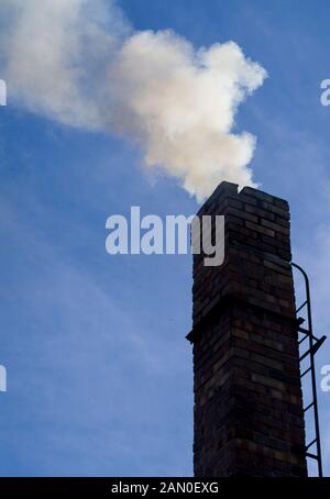 fumo in bilding / uscita dal camino di casa su sfondo cielo blu. Riscaldamento non ecologico delle famiglie. Riscaldamento invernale, oneri ambientali. Foto Stock