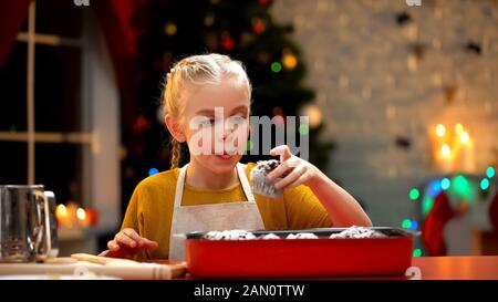 Ragazza carina mangiare muffin al cioccolato preparato per la vigilia di Natale, atmosfera di vacanza Foto Stock