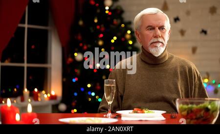 Uomo turbato seduto solo sul tavolo di Natale, nessun umore per festa Foto Stock