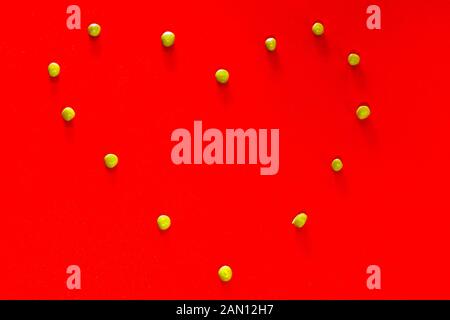 Bel cuore fatto di piccoli piselli verdi su uno sfondo rosso brillante Foto Stock