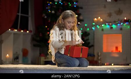 Cute ragazza apertura presente sotto albero di Natale, regalo da Santa, magia vigilia Foto Stock