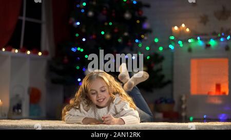 Piccola ragazza che scrive la lettera a Santa sdraiata sul pavimento, credenza nella fiaba magica Foto Stock