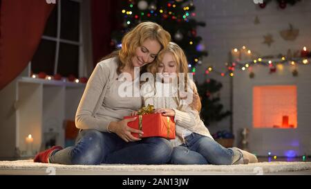 Piccola figlia che dona il presente alla madre amorevole, celebrando insieme il Natale Foto Stock