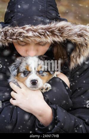 Bella ragazza adolescente tiene i suoi sei settimane vecchio piccolo cane nella neve all'esterno. Messa a fuoco selettiva sul pastore australiano cucciolo del viso. Egli ha un solo blu Foto Stock