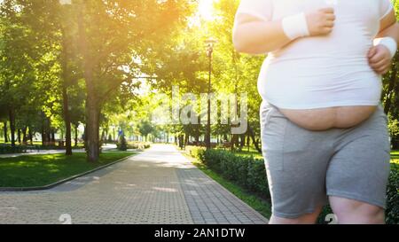 Obeso uomo jogging nel parco, persistente nel peso perdente, grande ventre vicino Foto Stock