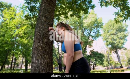 Giovane obesa signora stanco dopo il jogging, cardio workouts giornalieri per bruciare il grasso del ventre Foto Stock