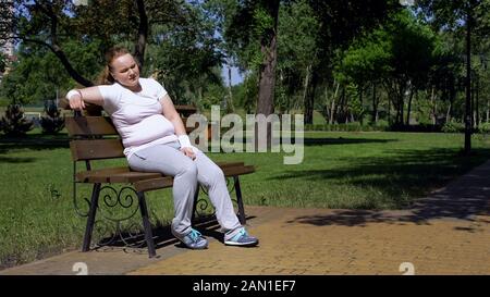 Fat ragazza seduta su panchina, stanco dopo l'allenamento nel parco, mancanza di motivazione Foto Stock