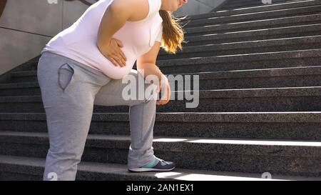 La ragazza grassa sente il dolore nello stomaco, il sovrappeso causa i problemi di salute, il dolore alla schiena Foto Stock