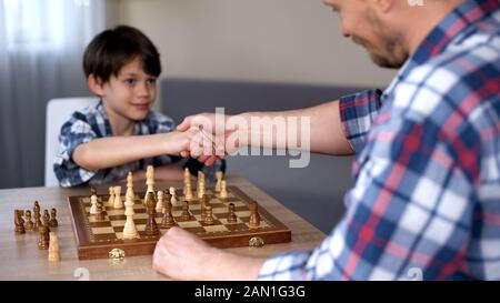 Cute geniale capretto vincente gioco di scacchi, handshaking con il suo padre orgoglioso, hobby Foto Stock