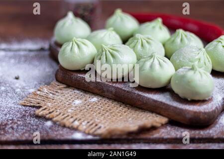 Pasta congelata khinkali con spinaci. Guarnito con peperoncino rosso, aneto e Prezzemolo. Su uno sfondo di legno. Spazio di copia. Foto Stock