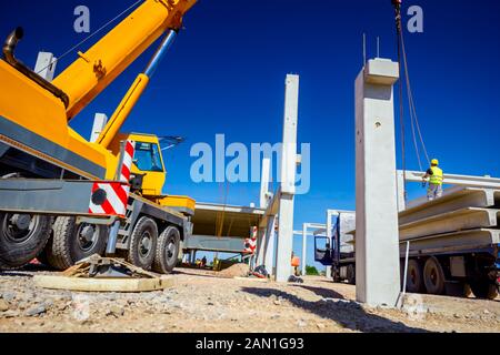 Lavoratore sta preparando il gancio della gru per lo scarico di un travetto in cemento da camion rimorchio. Foto Stock