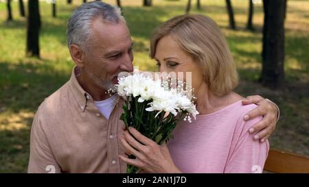 Bella donna invecchiato profumati fiori presentati man, vecchia coppia data nel parco, amore Foto Stock