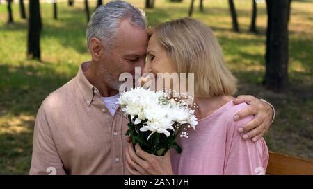 Amare di età matura nuzzling durante la data romantico nel parco, mazzo di fiori presente Foto Stock
