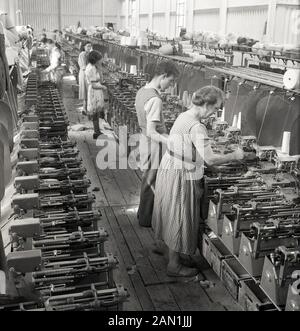 Degli anni Cinquanta, storico, maschio e femmina dei lavoratori tessili in piedi su assi di legno funzionante a telai di tessitura, utilizzando le macchine meccanizzate per produrre il tessuto, l'Irlanda del Nord. Foto Stock