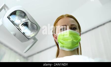 Signora terapeuta in maschera protettiva guardando al paziente, procedura di cosmetologia Foto Stock