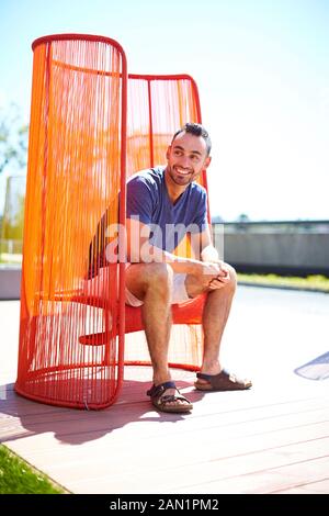 Un uomo seduto fuori in una sedia colorata e moderna. Foto Stock