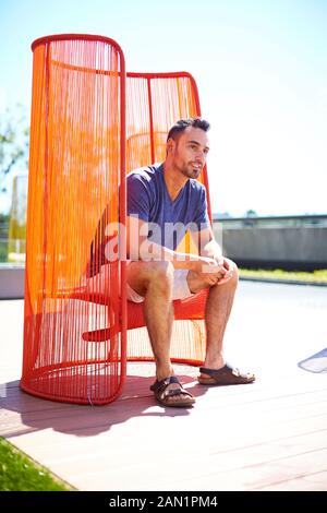 Un uomo seduto fuori in una sedia colorata e moderna. Foto Stock