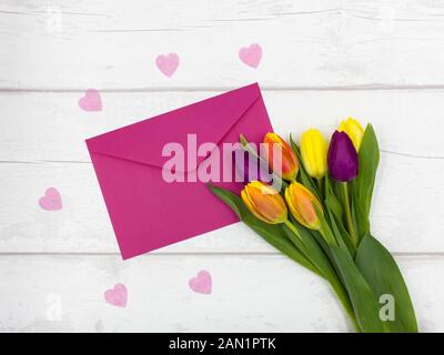 Vista superiore della bella colorata/Tulipani colorati, con una busta di colore rosa e Cuori rosa su un bianco tavolo rustico - madri/giorno di San Valentino Foto Stock