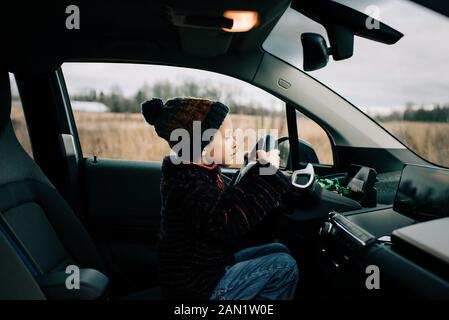 il ragazzo sedette nel sedile del conducente di un'auto elettrica che gioca Foto Stock